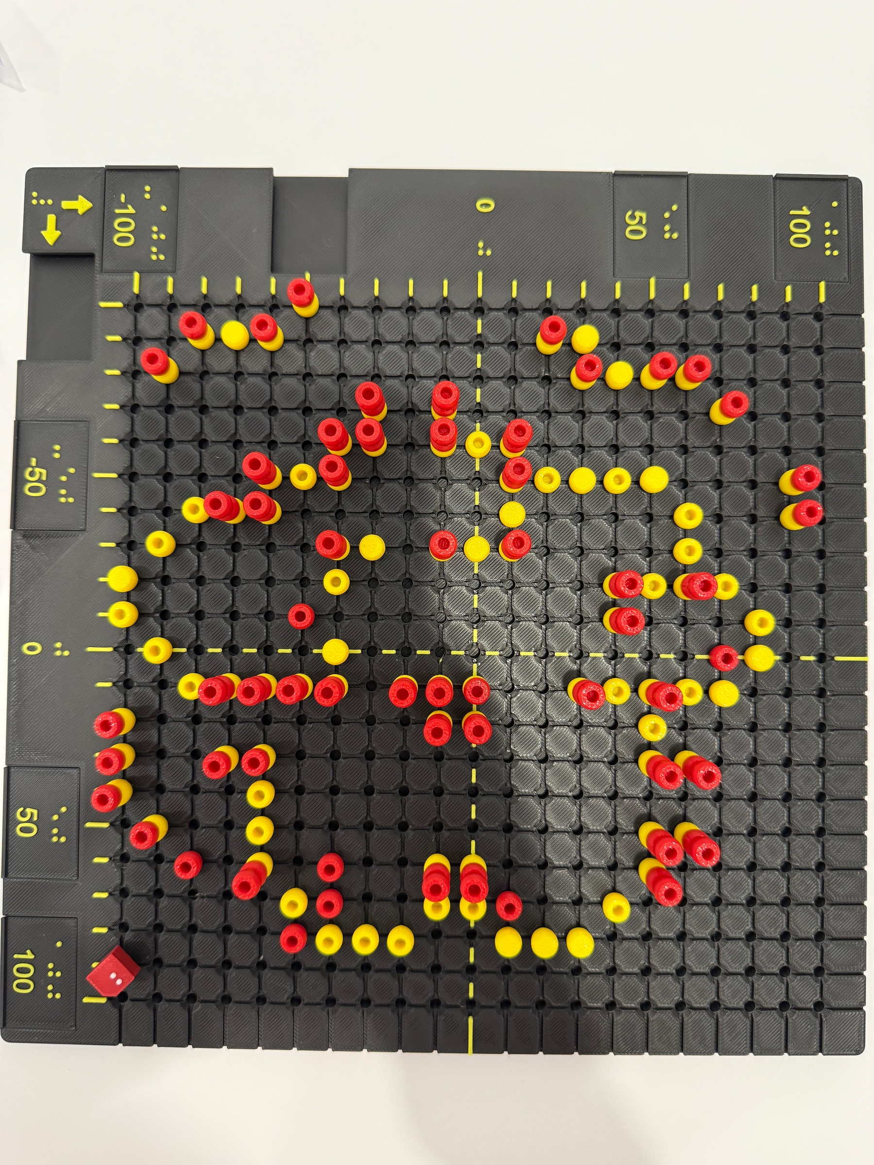 A tactile board with black pegs, featuring red and yellow pieces arranged in an architectural plan 
