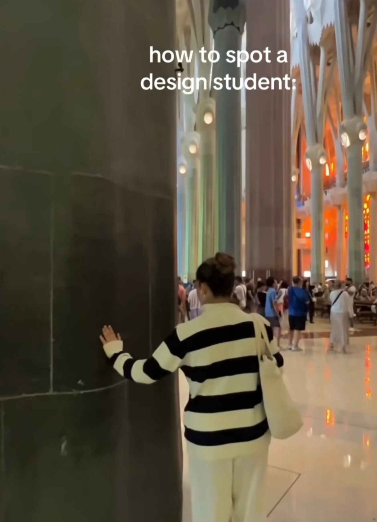 A person wearing a black and white striped sweater is touching a pillar inside a large, ornate building with colorful stained glass windows.