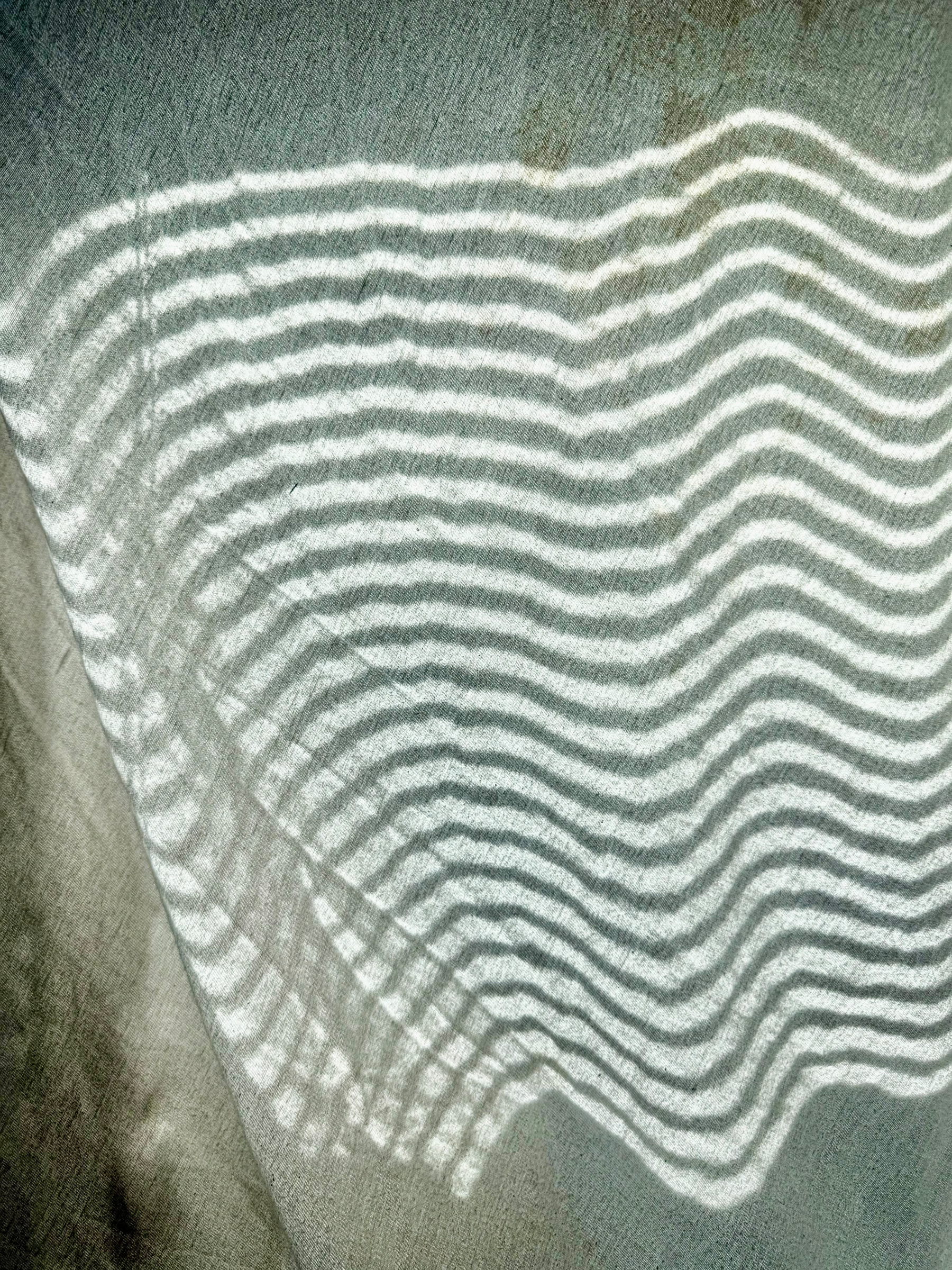 Soft, wavy lines of light on a fitted flannel sheet pulled loosely over a window frame. A warm, soft, cloth balloon. The room is cold. Light peeks through the slatted blinds, leaving lines of light to curl across the fabric.