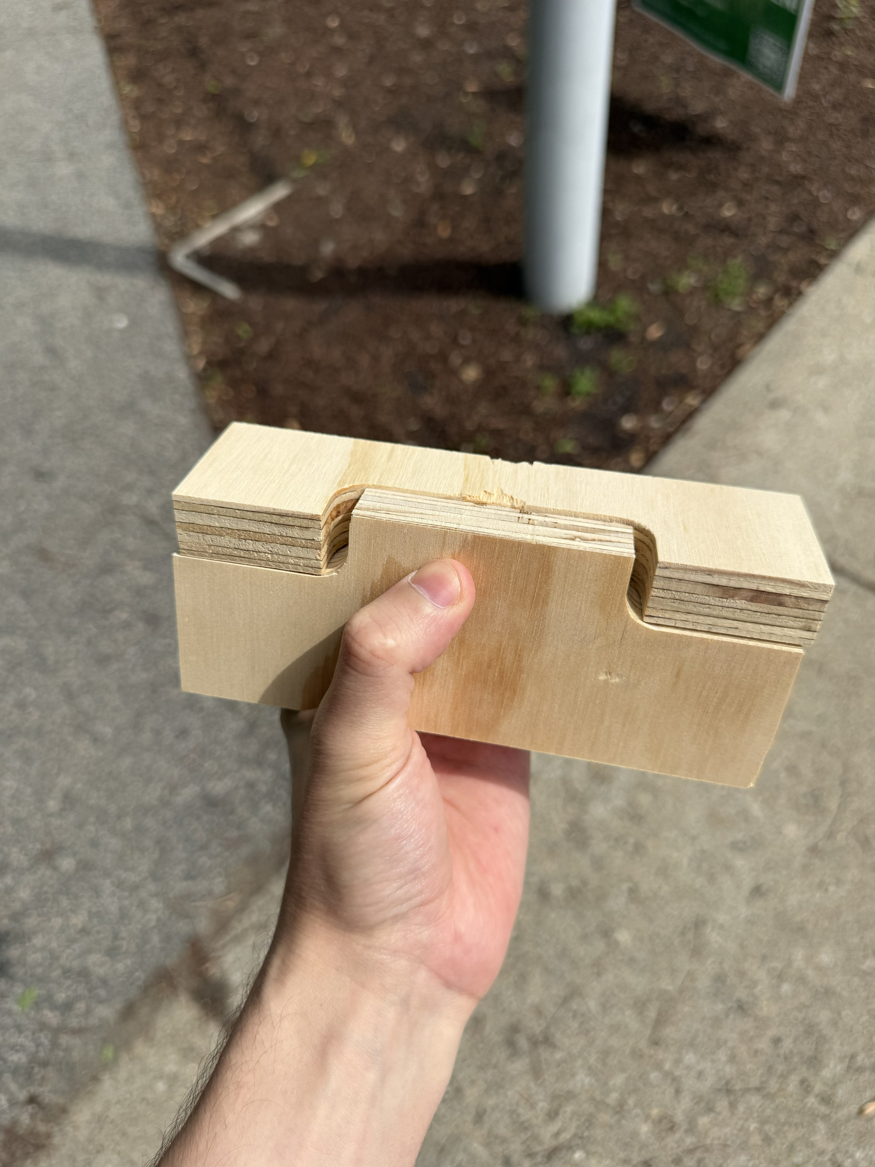 My hand is holding a wooden block with a notched design. I'm outside, on my walk home from the shop. 