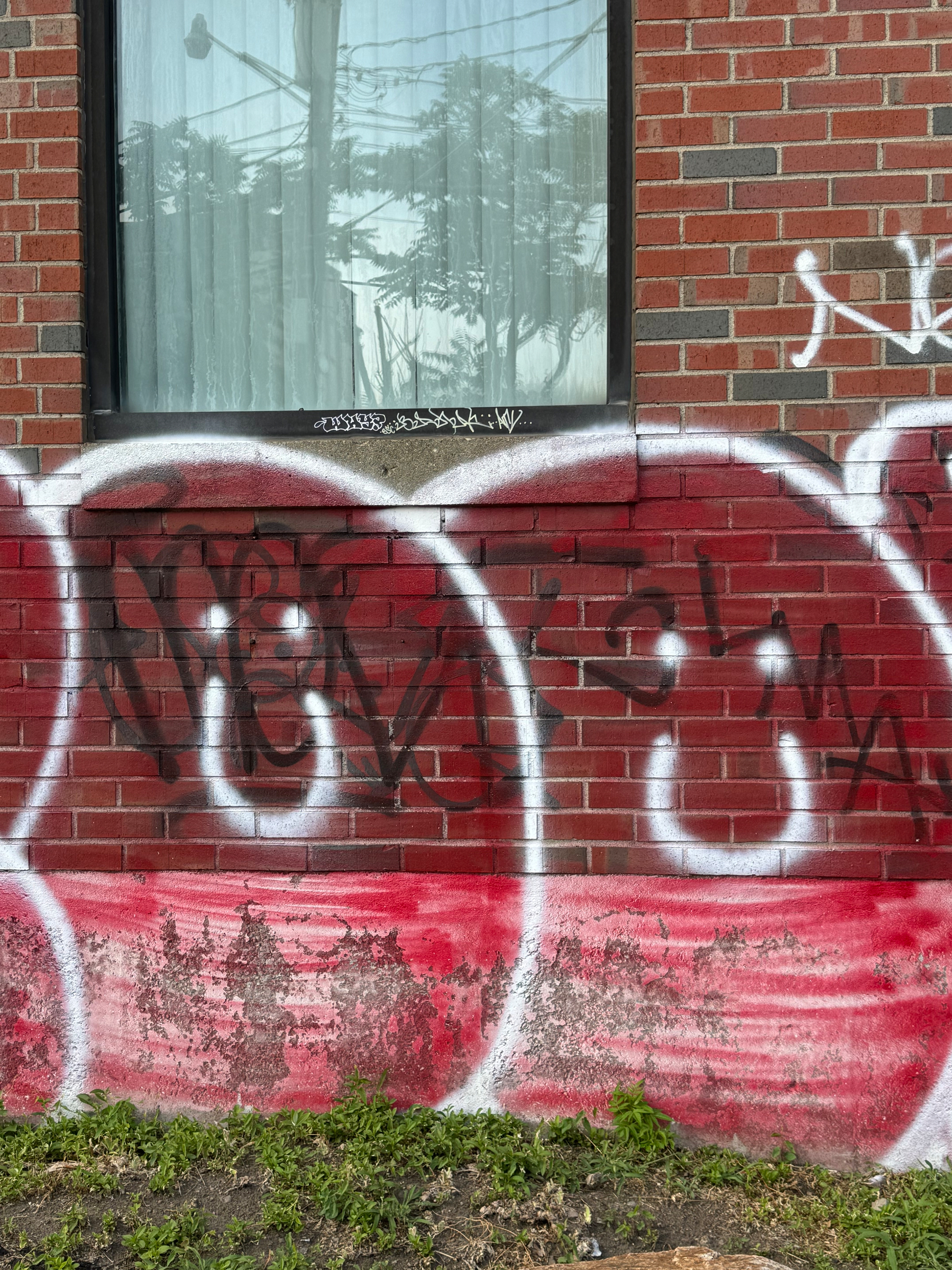 A brick wall with a window above is covered with graffiti painted in red, black, and white colors.
